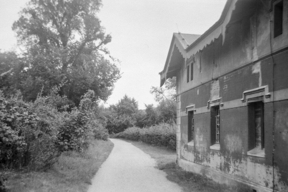 Schwarz-Weiss Foto zeigt einen Weg und ein alters Haus in einem Park, aufgenommen mit der Agfa Clack bei schlechtem Wetter