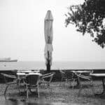 Schwarz-Weiß Foto zeigt Stühle und Tische im Regen, im Hintergrund ist ein Schiff auf dem nebeligen See zu sehen