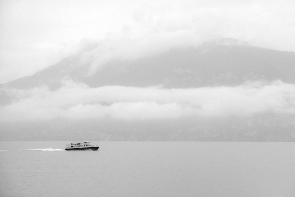 Schwarz-Weiß Foto des Gardasees, auf dem ein Schiff vor einem Berg mit vielen Wolken über den See fährt