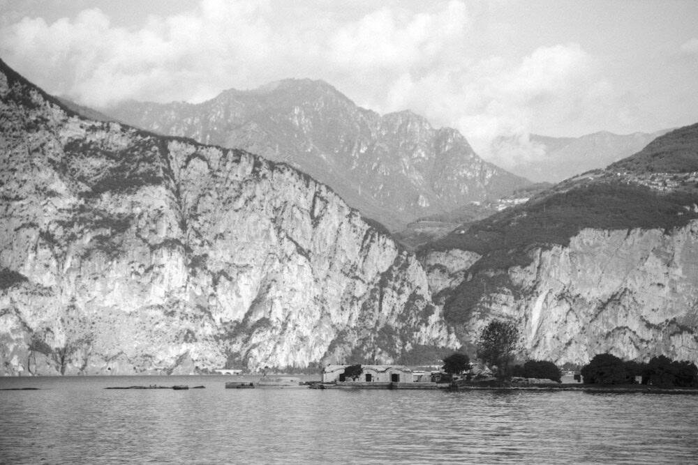Schwarz-Weiß Foto der Insel Isola di Trimelone im Gardasee in Italien, im Hintergrund sind Berge zu sehen