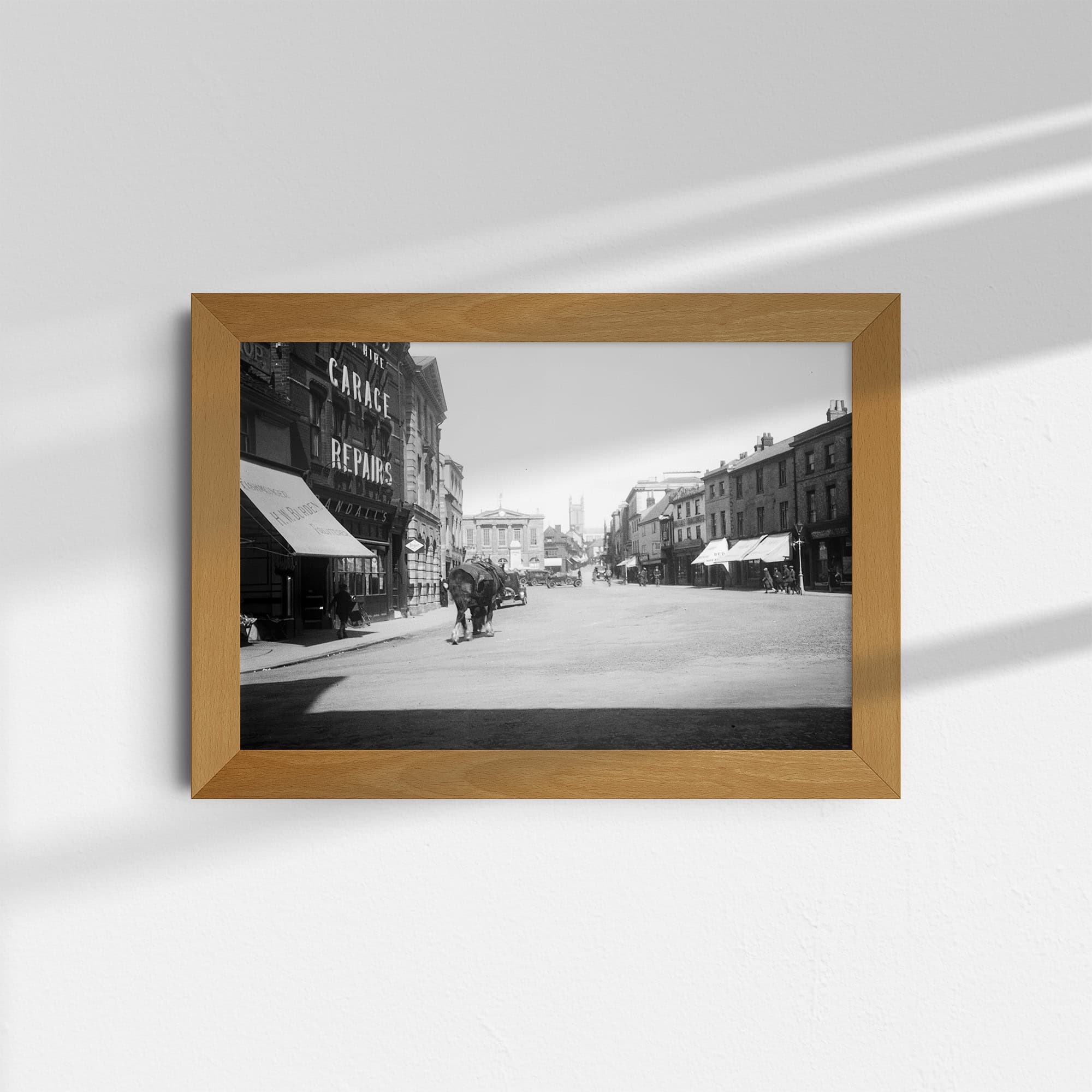 Dieses historische Schwarz-Weiß Foto zeigt die High Street in der Stadt Andover in Hampshire, England. Es wurde um das Jahr 1930 aufgenommen. Im Vordergrund sind Geschäfte zu sehen, im Hintergrund sind die Andover Guildhall und eine Kirche, die Church of St Mary.