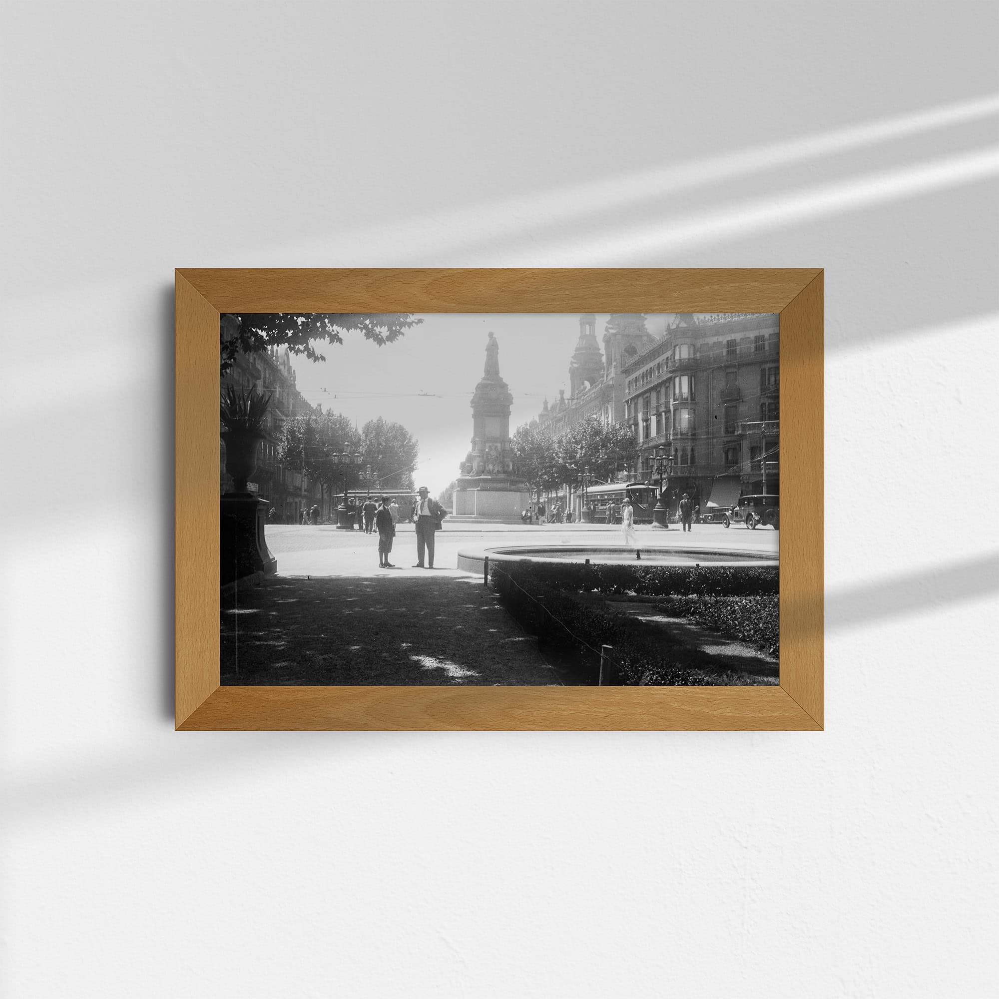 Dieses alte Schwarz-Weiß Foto zeigt eine Straßenszene in Barcelona um das Jahr 1930. Zu sehen ist die Kreuzung Gran Vía und Rambla de Catalunya mit dem alten Denkmal für Joan Güell i Ferrer, das im Jahr 1936 zerstört wurde. Im Vordergrund unterhalten sich zwei Männer. Es sind alte Straßenbahnen und Autos zu sehen.