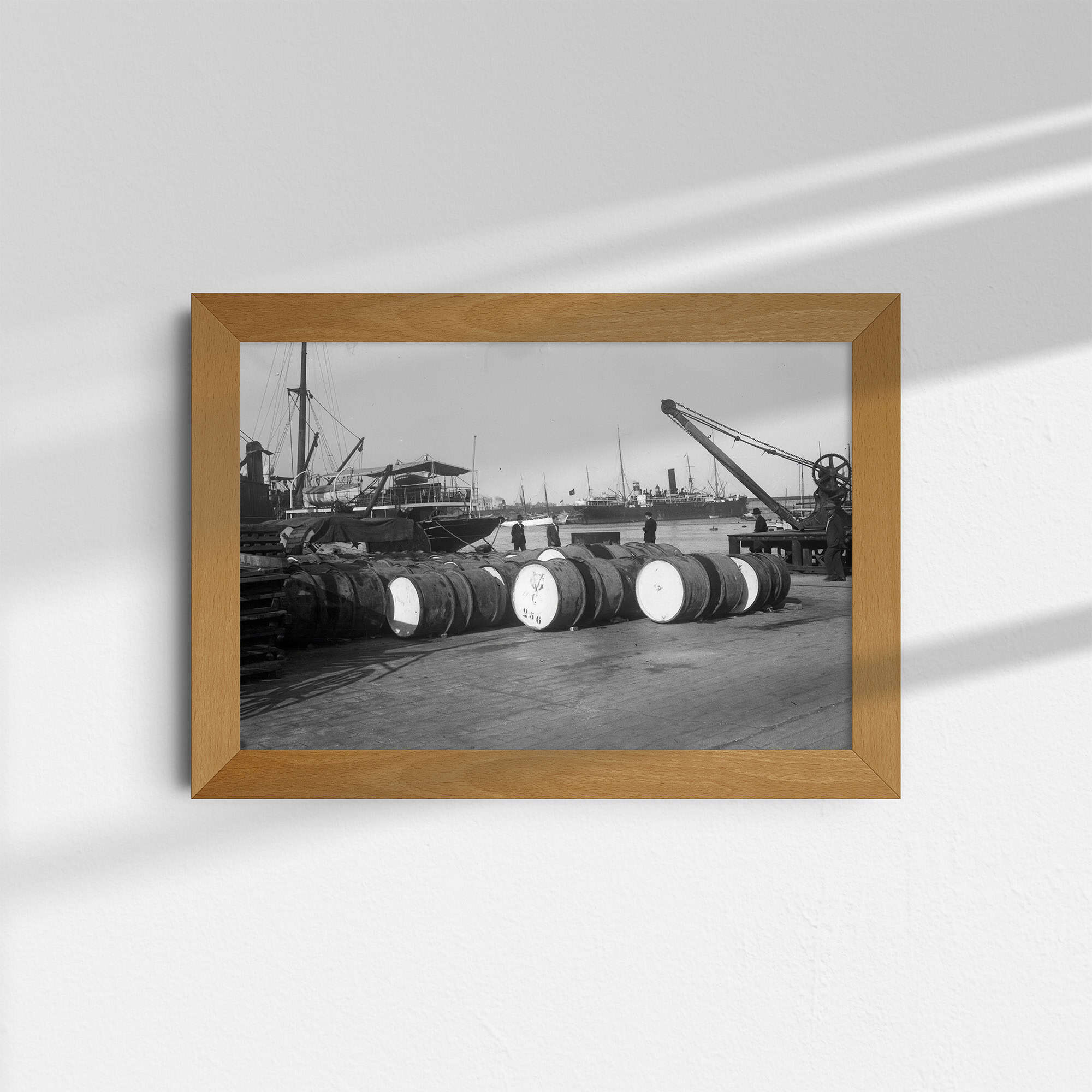 Dieses alte Schwarz-Weiß Foto zeigt eine Szene aus einem großen Hafen. Im Vordergrund lagern Güter auf dem Kai, im Hintergrund sind Schiffe und ein Kran zu sehen. Die Fotografie wurde um das Jahr 1930 in Barcelona aufgenommen. Dieses und weitere Bilder biete ich bei AtticPhotos an.