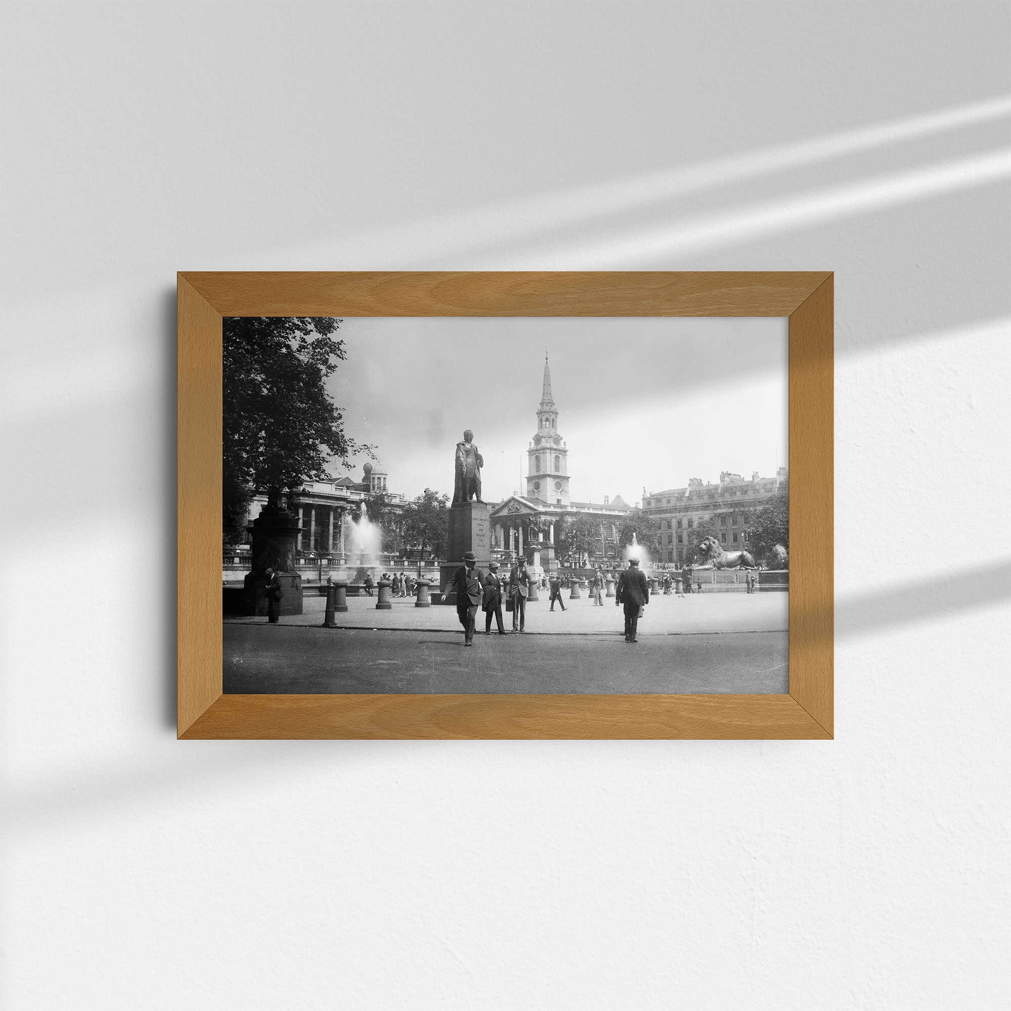 Dieses alte Schwarz-Weiß Foto zeigt den Trafalgar Square in London. Im Vordergrund ist die Nelson-Säule zu sehen, im Hintergrund die Kirche St. Martin-in-the-Fields. Das Foto wurde um das Jahr 1930 aufgenommen.