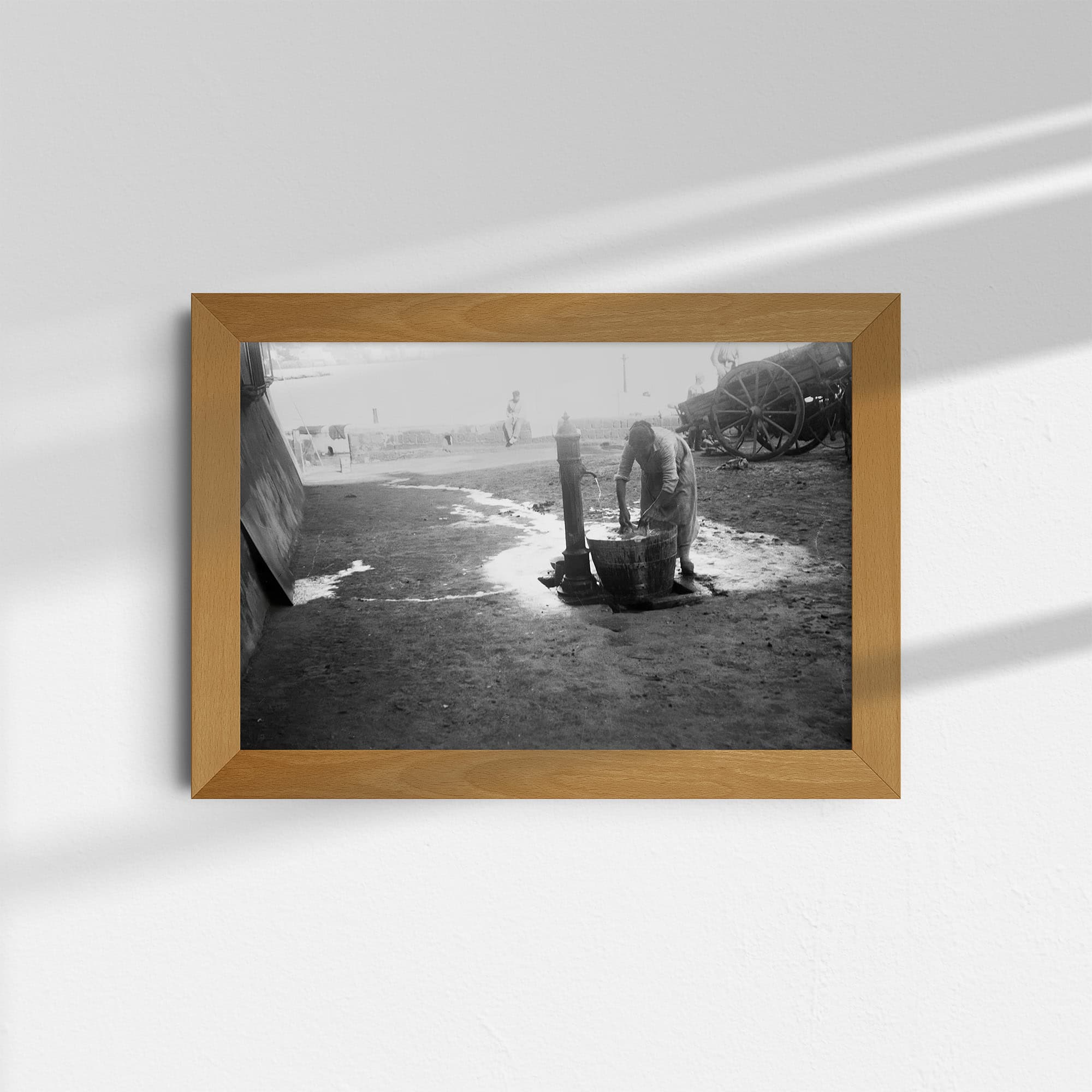 Dieses alte Schwarz-Weiß Foto zeigt eine Frau, die auf der Straße ihre Wäsche wäscht. Sie hat dazu einen Holzbottich an eine öffentliche Pumpe gestellt. Der Ort der Aufnahme ist unbekannt. Das Foto wurde um das Jahr 1930 aufgenommen.