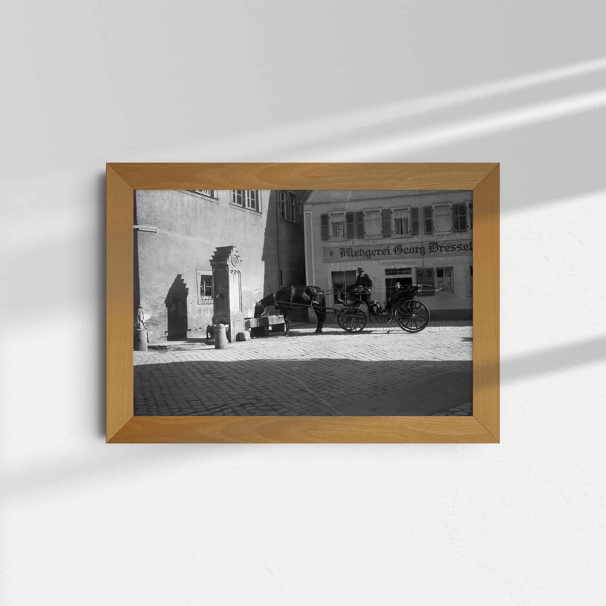 Dieses alte Schwarz-Weiß Foto zeigt eine Straßenszene, die in Heidingsfeld bei Würzburg, Deutschland, um das Jahr 1930 aufgenommen wurde. Eine von einem Pferd gezogene Kutsche hält an dem historischen Brunnen am Rathaus, um das Tier trinken zu lassen. Dieses und weitere Bilder biete ich bei AtticPhotos an. 