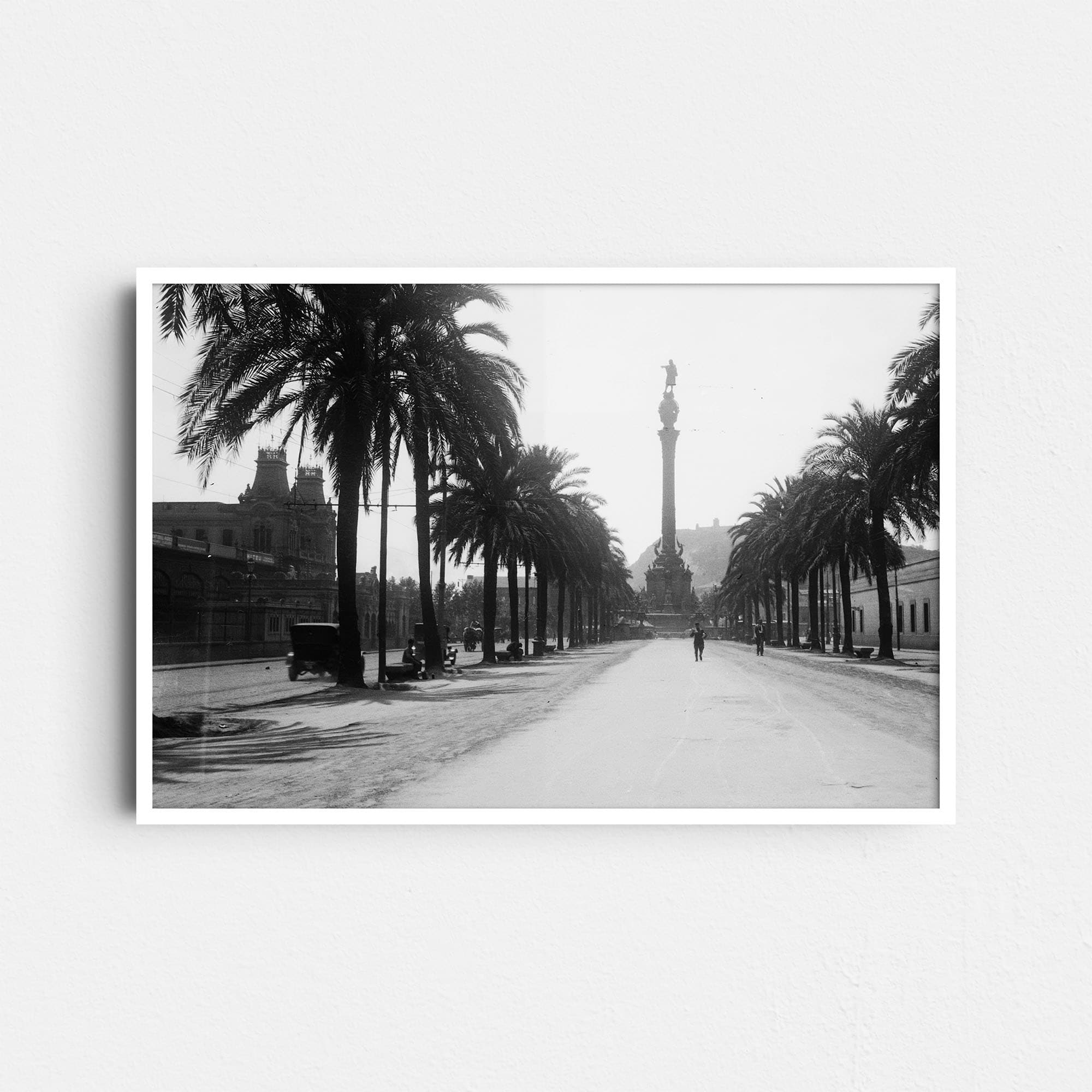 Dieses historische Foto zeigt den Passeig de Colom in Barcelona, Spanien, mit dem markanten Kolumbus-Denkmal (Monumento a Colón) im Hintergrund. Es wurde um das Jahr 1930 aufgenommen. Auf dem Bild sind Männer und ein historisches Fahrzeug zu sehen.