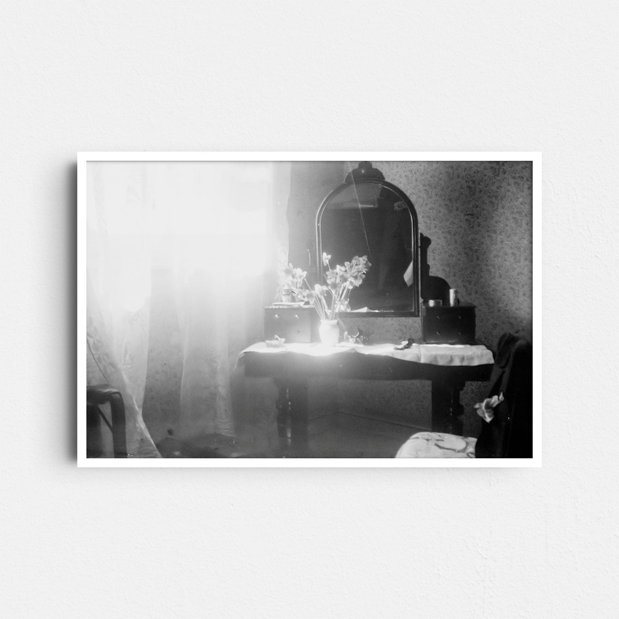 Dieses Schwarz-Weiß Foto zeigt einen alten Frisiertisch mit Spiegel, wie er in den 20er Jahren genutzt wurde. Auf dem Tisch steht eine Vase mit Blumen. Rechts ist ein Stuhl zu sehen, auf dessen Lehne ein Jackett hängt. Auf der linken Seite ist ein Fenster, durch das helles Tageslicht in das Zimmer fällt. Links unten sind Koffer zu sehen. Das Foto wurde wahrscheinlich in einem Zimmer des Hotels Ritz in Barcelona, Spanien, um das Jahr 1930 aufgenommen.