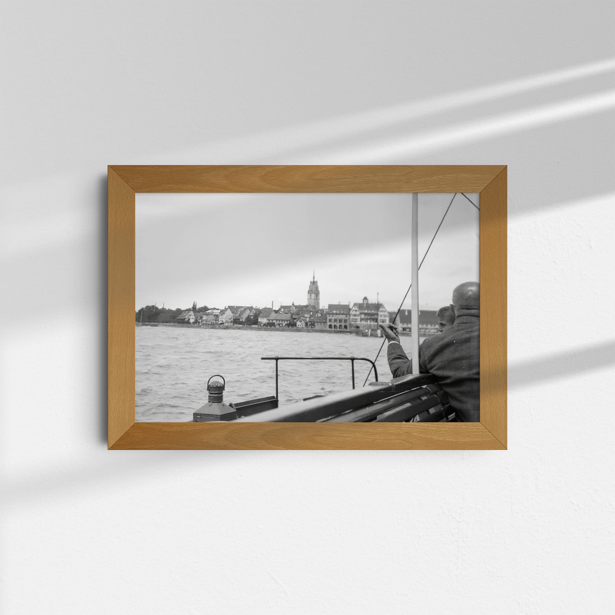 Dieses historische Foto zeigt eine Ansicht der Stadt Friedrichshafen vom Bodensee aus. Das Bild bietet einen Blick auf die Uferpromenade und die charakteristische Skyline der Stadt. Im Hintergrund ist die Schlosskirche zu sehen, die als barockes Wahrzeichen der Stadt gilt. Das Foto wurde ca. 1930 von einem Passagierschiff aus aufgenommen.