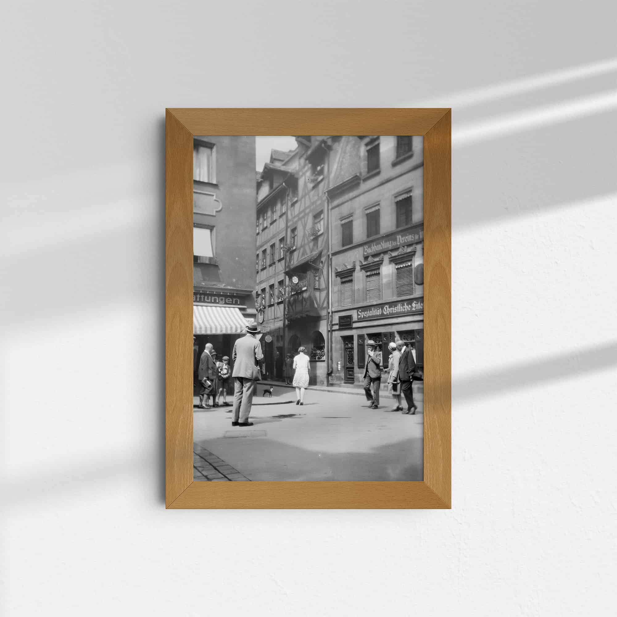 Dieses historische Schwarz-Weiß Foto zeigt einen Blick in die Hans-Sachs Gasse in der Nürnberger Altstadt. Im Zentrum ist das Hans-Sachs-Haus zu sehen, in dem der berühmte Dichter, Schuster und Meistersinger wohnte und arbeitete. Das Haus wurde im 2. Weltkrieg zerstört und nicht wieder aufgebaut. Im Vordergrund sind Passanten zu sehen.