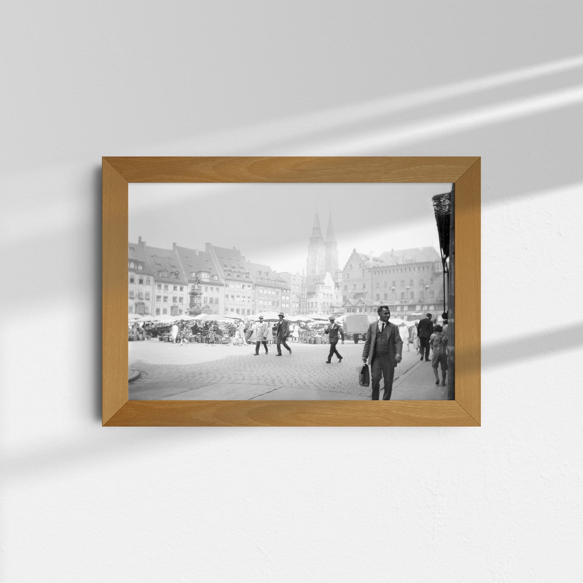 Diese historische Schwarz-Weiß Fotografie zeigt den Hauptmarkt in Nürnberg mit den Türmen der St. Sebaldus-Kirche im Hintergrund. Auf dem Markt sind viele Stände aufgebaut, zwischen denen Menschen zu sehen sind. Im Vordergrund sind Passanten zu sehen. Das Foto wurde in den 1920er oder 1930er Jahren aufgenommen.