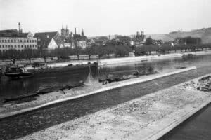 Dieses historische Schwarz-Weiß Foto zeigt den Fluss Main bei Würzburg um das Jahr 1930. Auf dem Fluss sind Lastkähne zu sehen, am Würzburger Ufer ist eine Möbelfabrik. Im Hintergrund ist der Dom zu erkennen.