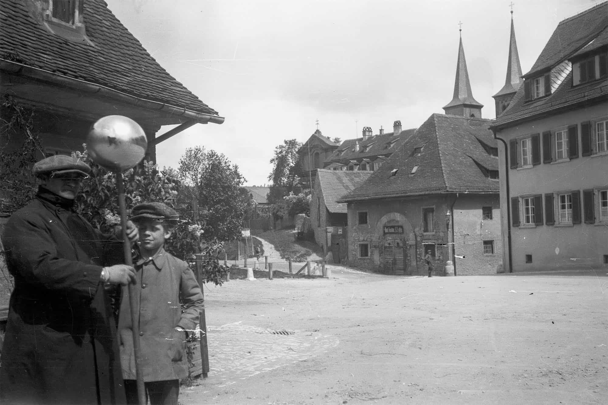 Dieses historische Schwarz-Weiß Foto wurde um das Jahr 1930 in Würzburg aufgenommen. Es zeigt alte Gebäude in der Nähe des Zeller Tores. im Hintergrund sind die Kirchtürme der heutigen Don-Bosco-Kirche. Am linken Bildrand stehen ein Mann und ein Junge und schauen zum Fotografen.